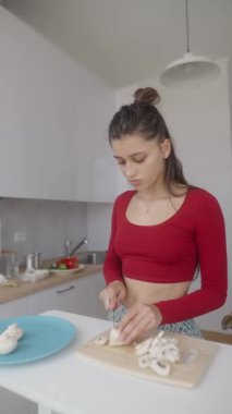 Genç bir kadın parlak, modern bir mutfakta ustaca mantar doğruyor ve yemek pişirme yeteneğini sergiliyor..