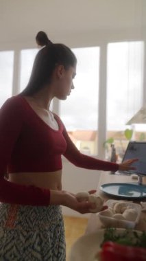 Yemek pişiren, yemek tariflerini araştıran ve parlak bir mutfakta taze malzemeler hazırlayan bir kadın..