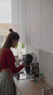 Bir kadın, doğal ışık ve canlı bitkilerle dolu şık bir mutfakta lezzetli yemekler hazırlıyor.