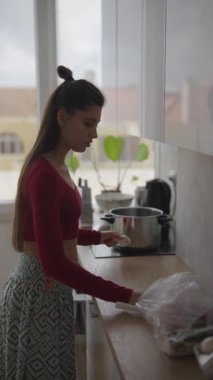 Genç bir kadın, güneş ışığı ve tarzla dolu parlak, modern bir mutfakta neşeyle lezzetli yemekler hazırlıyor.