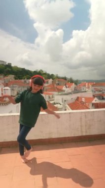 Genç bir insan neşeyle çatıda dans ediyor, kulaklıkla çarpıcı manzaranın ve neşeli müziğin tadını çıkarıyor.