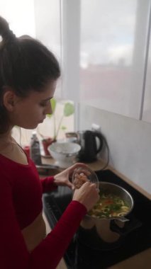 Genç bir kadın şık mutfağında besleyici bir sebze çorbası hazırlıyor..