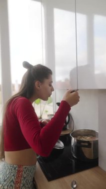 Şık ve modern bir mutfakta genç bir kadın lezzetli yemeklerini kaşıkla tadıyor, anın tadını çıkarıyor.