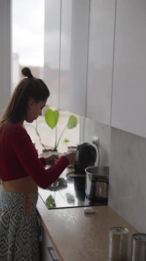 Modern mutfağında, bir kadın doğal ışıkla aydınlatılmış lezzetli bir fincan kahve yapıyor.