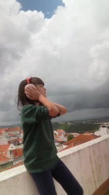 Genç bir çocuk kulaklarını doğal seslerden korurken dışarıda güzel bir ortamda müzik dinliyor.