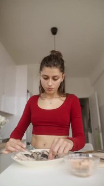 Kırmızı bluzlu odaklanmış genç bir kadın evde yemek hazırlıyor. Mutfak becerileri ve yaratıcılığını gösteriyor..