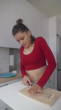 Canlı kırmızı bir bluz giymiş genç bir kadın zarif bir mutfakta ustaca ve mutlu bir şekilde lezzetli yemekler hazırlıyor.