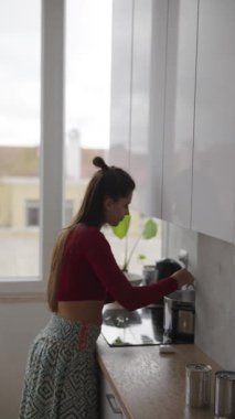 Doğal ışık ve canlı bitkilerle dolu modern bir mutfakta, bir kadın ustaca bir yemek hazırlar.