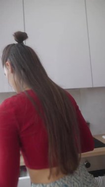 Modern bir mutfakta, genç bir kadın yemek pişirme yeteneklerini sergileyerek taze malzemeler hazırlar.