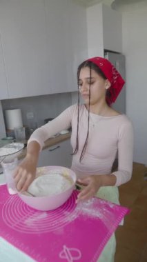 Genç bir kadın renkli bir mutfakta hamuru zevkle hazırlıyor. Yemek pişirme becerilerini sergiliyor.