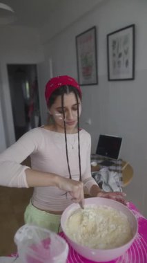 Parlak bir mutfakta, genç bir kadın farklı malzemeler karıştırarak pişirme sanatını zevkle icra eder.