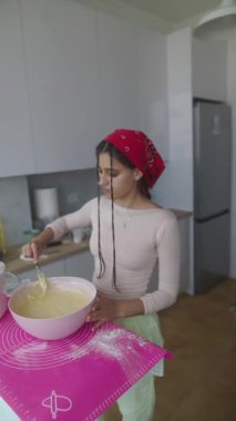 Genç bir kadın parlak mutfağında kek hamuru hazırlıyor ve etkileyici pişirme becerilerini sergiliyor.