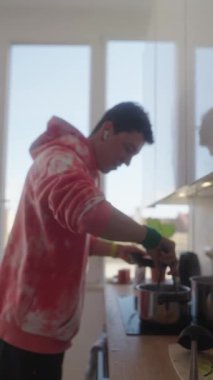 Genç bir adam şık bir mutfakta ustalıkla yemek pişiriyor, canlı bir kazak giyiyor ve mutfak sürecinin tadını çıkarıyor..