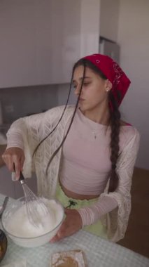 Genç bir kadın, taze yiyeceklerle çevrili, mutfak yaratıcılığını gösteren parlak bir mutfakta bir kase karıştırıyor..