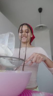 Neşeli bir fırıncı, parlak bir mutfakta ustalıkla tatlı yaparak şekeri bir kaseye karıştırıyor.