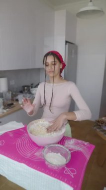 Genç bir kadın, taze malzemelerle dolu parlak bir mutfakta hamuru ustalıkla karıştırmaktan hoşlanır.