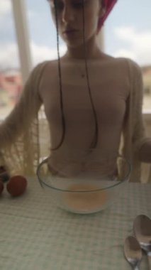 Bir kişi büyük bir kaseye çeşitli malzemeler ekleyerek pişirme oturumuna hazırlanıyor. İçeride yemek pişirme sahnesi