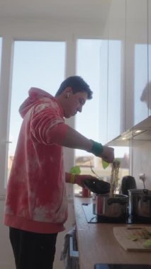 Genç bir adam güzel doğal ışıkla dolu parlak ve modern bir mutfakta ustalıkla lezzetli bir yemek hazırlar.