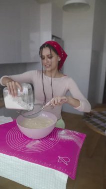 Parlak bir mutfakta, genç bir kadın bir kaseye un dökerek ustalıkla lezzetli bir hamur hazırlar.