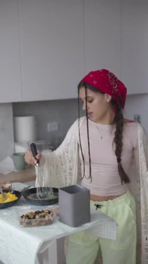 Şık mutfağında, parlak kırmızı bir bandana takan genç bir kadın neşeyle lezzetli bir yemek hazırlıyor.