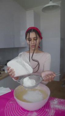 Genç bir kadın büyük bir karıştırma kabına ustalıkla un ekler, ev yemeğinin saf neşesini ve zevkini somutlaştırır.