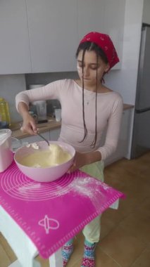 Genç bir kadın büyük bir kâsede taze hamuru karıştırarak neşeli mutfağında enfes bir pişirme anını yakalıyor.