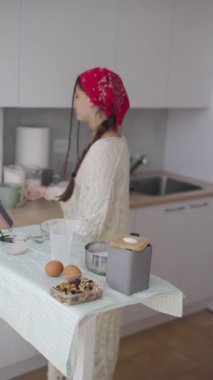 Parlak bir mutfakta renkli bir başörtüsü olan bir kadın, taze malzemeler kullanarak ustalıkla yemek hazırlıyor.