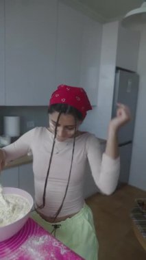 Neşeli bir kadın stil mutfağında hamuru coşkuyla karıştırıyor, gerçek bir aşkla yemek pişiriyor.