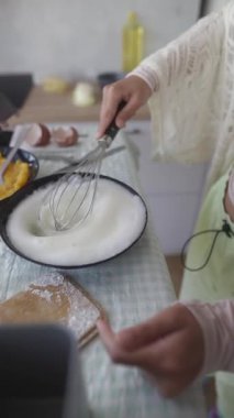 Bir insan, yaratıcı malzemelerle çevrili şık bir mutfakta çırpıcıyla krema çırpar.