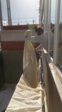 Bir insan, balkonda dikilirken parlak ve güneşli bir ortamda çarşafları titizlikle tutar.