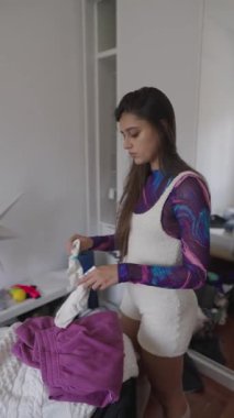 Genç bir kadın şık bir iç mekan ortamında canlı giysiler organize ediyor, benzersiz moda anlayışını sergiliyor..