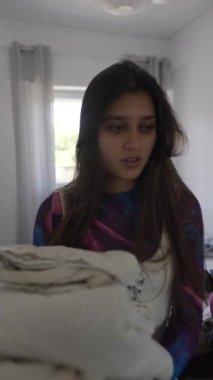 Genç bir kadın renkli yatak odasını topluyor, katlanmış çarşaflar taşıyor ve huzurlu bir sabah rutininin tadını çıkarıyor.