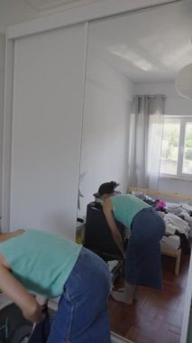 Bir insan, sıcak, güneşli ve neşeli bir yatak odası ortamında kıyafetlerini topluyor.