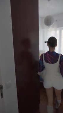 Bir manken şık bir odada gezer, canlı bir ortam seyrederken canlı kıyafetler giyer.