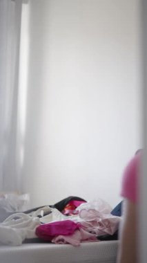 Pembe şortla birlikte dar bir tişört giyen genç bir kadın düşünceli bir şekilde iç mekanda poz veriyor.