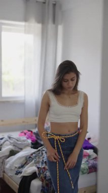 Genç bir kadın rahat, parlak bir odada rahat kıyafetlerini şekillendirirken kendine güvenerek poz veriyor.
