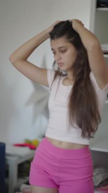 Genç bir kadın parlak renkli bir kıyafet içinde, güne hazırlanırken dolabını incelikle düzenliyor.