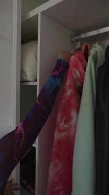 Şık bir birey titiz bir şekilde canlı giysiler ve aksesuarlarla dolu bir dolabın içinden geçiyor.