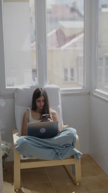 Genç bir kadın dizüstü bilgisayarına derinden odaklanmıştır. İşine sıcak, güneşli bir oda ortamında dalmıştır.