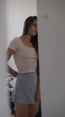 Parlak bir yatak odasında, genç bir kadın şık ve rahat görünümünü sergilemek için şık kıyafetini ayarlıyor.