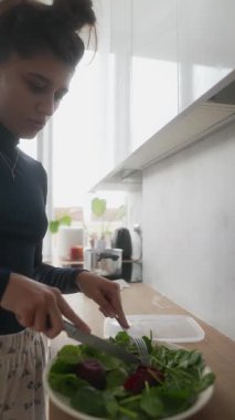 Bir kadın yetenekli bir şekilde canlı bir salata hazırlar. Parlak bir mutfakta sebze ve pancarı birleştirir. Yeteneğini gösterir.