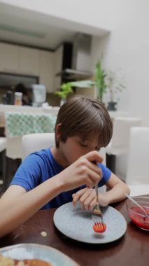 Genç bir çocuk, taze meyve salatası ve pofuduk kreplerden oluşan lezzetli yemeğine odaklanmış bir şekilde kahvaltısının tadını çıkarıyor.