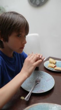 Genç bir çocuk, yemek masasında otururken lezzetli ve lezzetli bir aperatifin tadını çıkarıyor.