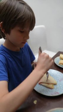 Genç bir çocuk enerji dolu bir şekilde yemek masasında büyük bir coşkuyla leziz kreplerin tadını çıkarıyor.
