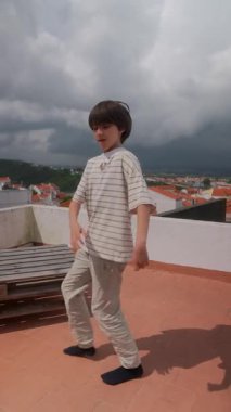 Genç bir çocuk, üzerindeki dramatik, girdap gibi bulutlara hayret ederken çatıda oyun zamanının keyfini çıkartıyor.