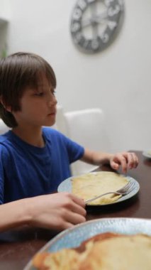 Aile masasında ev yapımı kreplerin tadını çıkaran genç bir çocuk sevdikleriyle yemek yediği keyifli anlar sergiliyor.