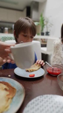 Genç bir çocuk, leziz kreplerin tadını çıkarıyor. Renkli reçelle kaplanmış, samimi ve davetkar bir yemek düzeninde.