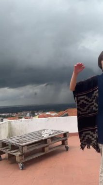 Yetenekli genç bir sanatçı çatıdaki fırtınalı gökyüzüne karşı bir dizi duygu sergiliyor.