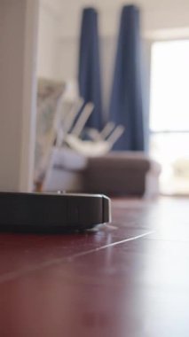 Parlatılmış ahşap zemin üzerinde, arka planda rahat bir yaşam alanı olan robotik bir elektrikli süpürgenin yakın çekimi..