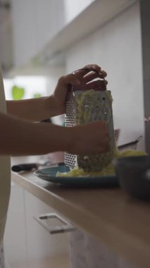 Şık bir mutfakta taze ve renkli malzemeler hazırlamak için bir kutu rendesini ustaca kullanan ellerin yakın plan görüntüsü.